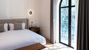 A bedroom with a large bed, a bedside table, a lamp, and a window with curtains. - Casa Lerma (Mexico City)