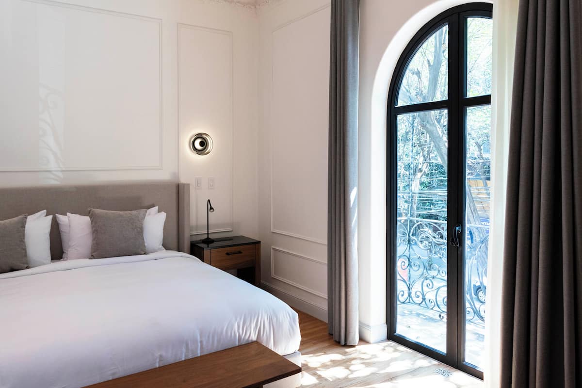 A bedroom with a large bed, a bedside table, a lamp, and a window with curtains.