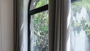 A room with a wooden chair, a black ottoman, and a window with curtains. - Casa Lerma (Mexico City)