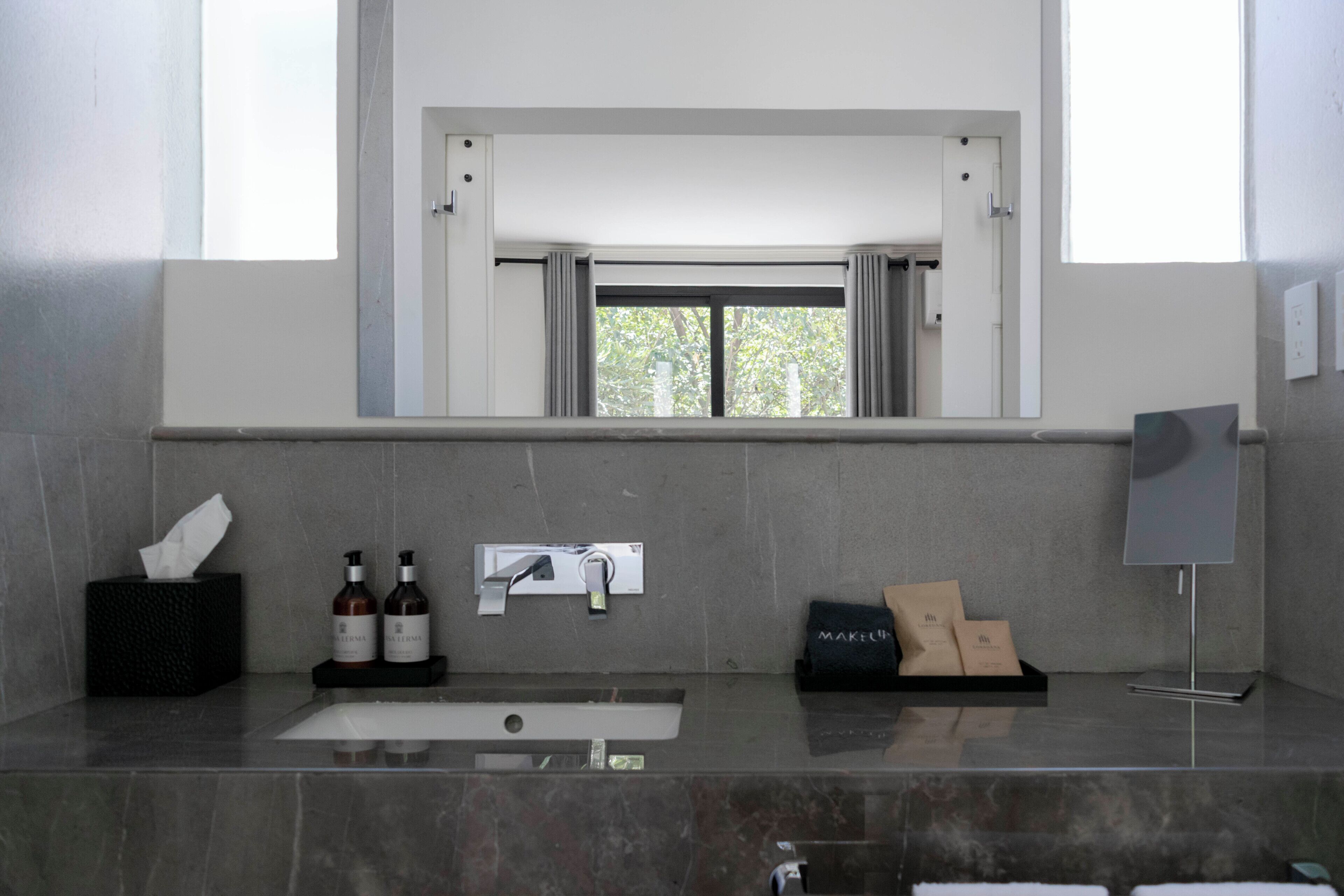 Un baño moderno con un espejo grande, un lavabo y una ventana sobre el espejo.