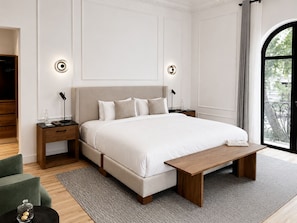 Un dormitorio moderno con una cama grande, mesitas de noche, un banco y vistas a la vegetación.