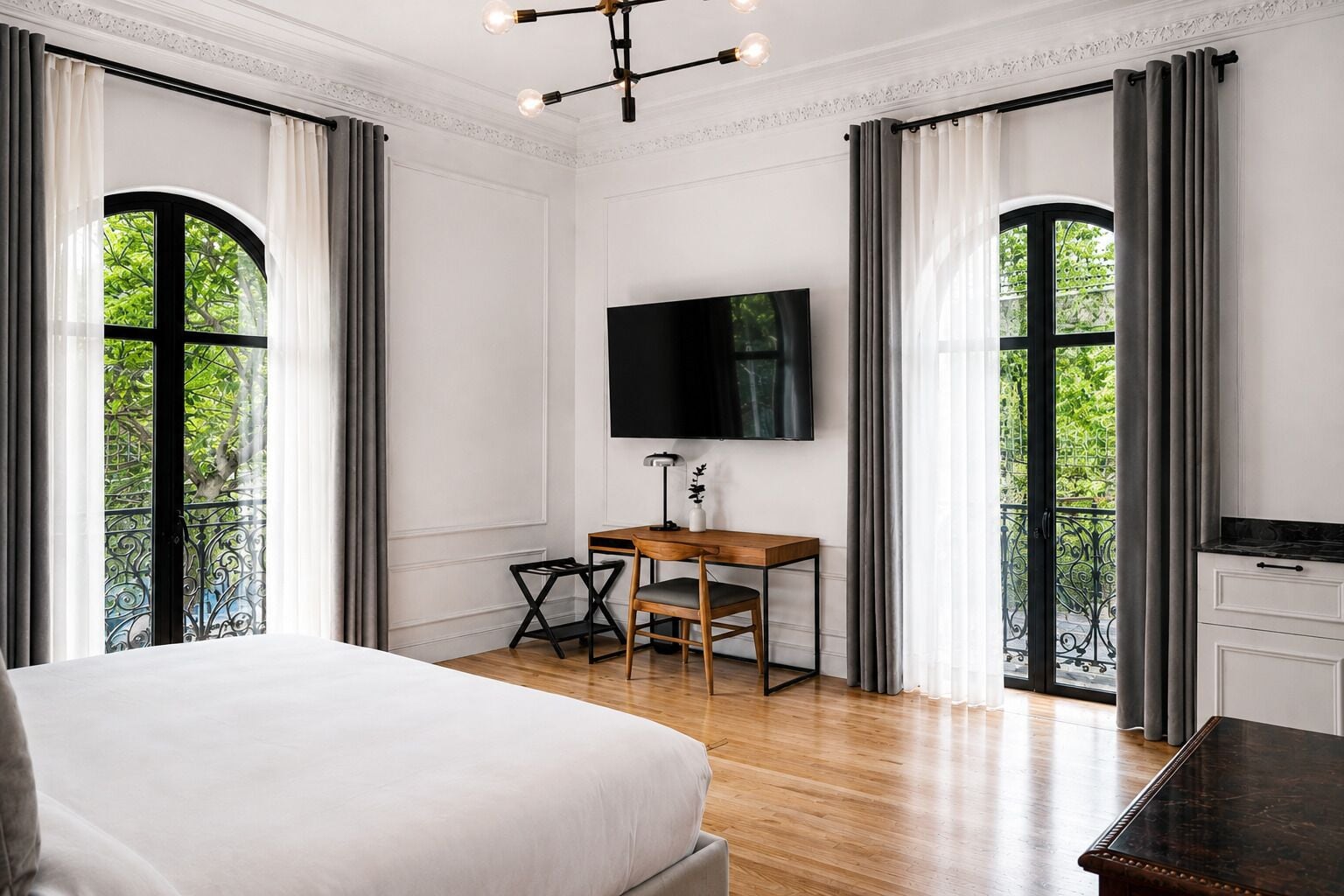 Habitación de hotel con una cama grande, un escritorio con una silla, un televisor de pantalla plana y ventanas amplias con cortinas.