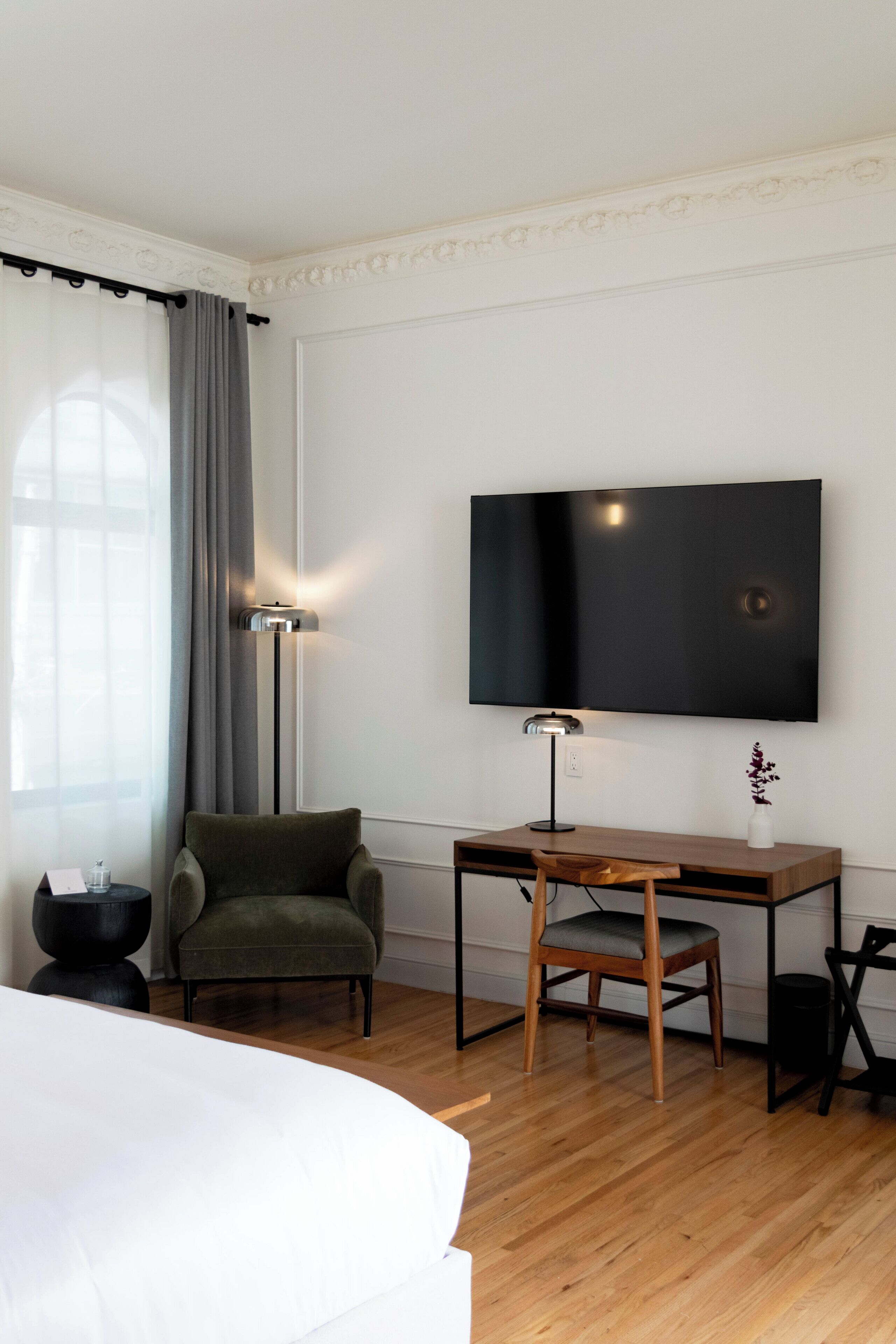 A hotel room with a bed, a desk, a chair, a TV, a lamp, and a window with curtains.