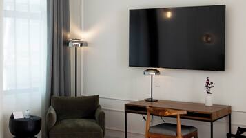 A hotel room with a bed, a desk, a chair, a TV, a lamp, and a window with curtains.