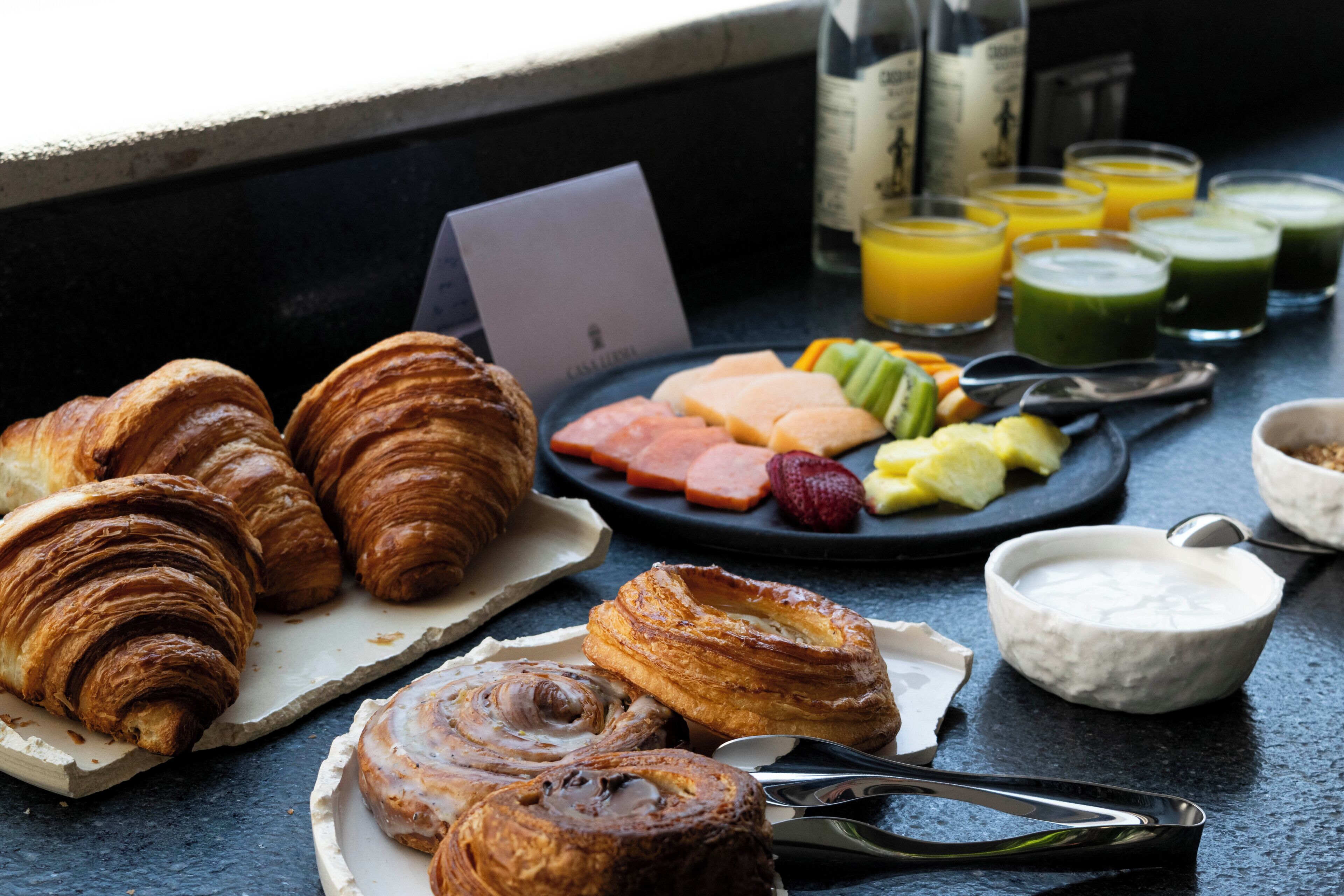 En frukostbuffé med bakverk, frukt och drycker uppdukad på ett bord.