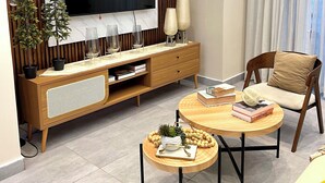 Un salon moderne doté d’un grand téléviseur à écran plat, de meubles en bois, d’une table basse ronde et d’un coin salon confortable.