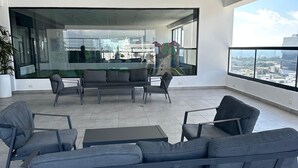 Un espace extérieur moderne, aménagé avec un canapé et des fauteuils, une cloison en verre et une vue sur la ville.