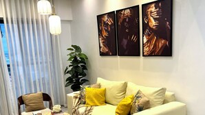 Un salon moderne avec un canapé, une table basse et un fauteuil. Il y a trois tableaux au mur et une grande plante.