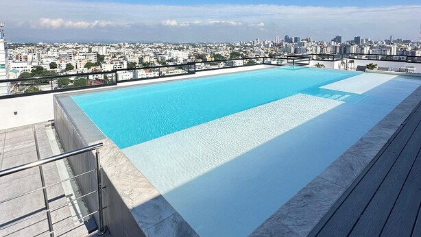 Une piscine sur le toit offrant une vue sur la ville, entourée d’une terrasse en bois et d’une rambarde en métal.