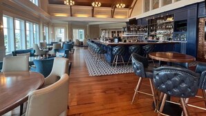 A spacious bar area with high ceilings and large windows, a bar counter with stools, and a seating area with tables and chairs. - Sunsets on Sealoft by Sandpiper | Near Beach (Seabrook Island)