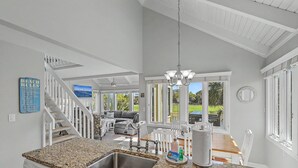 A kitchen with granite countertops, a stainless steel sink, a dining area with a wooden table and chairs, and a staircase with white railings. - Sunsets on Sealoft by Sandpiper | Near Beach (Seabrook Island)