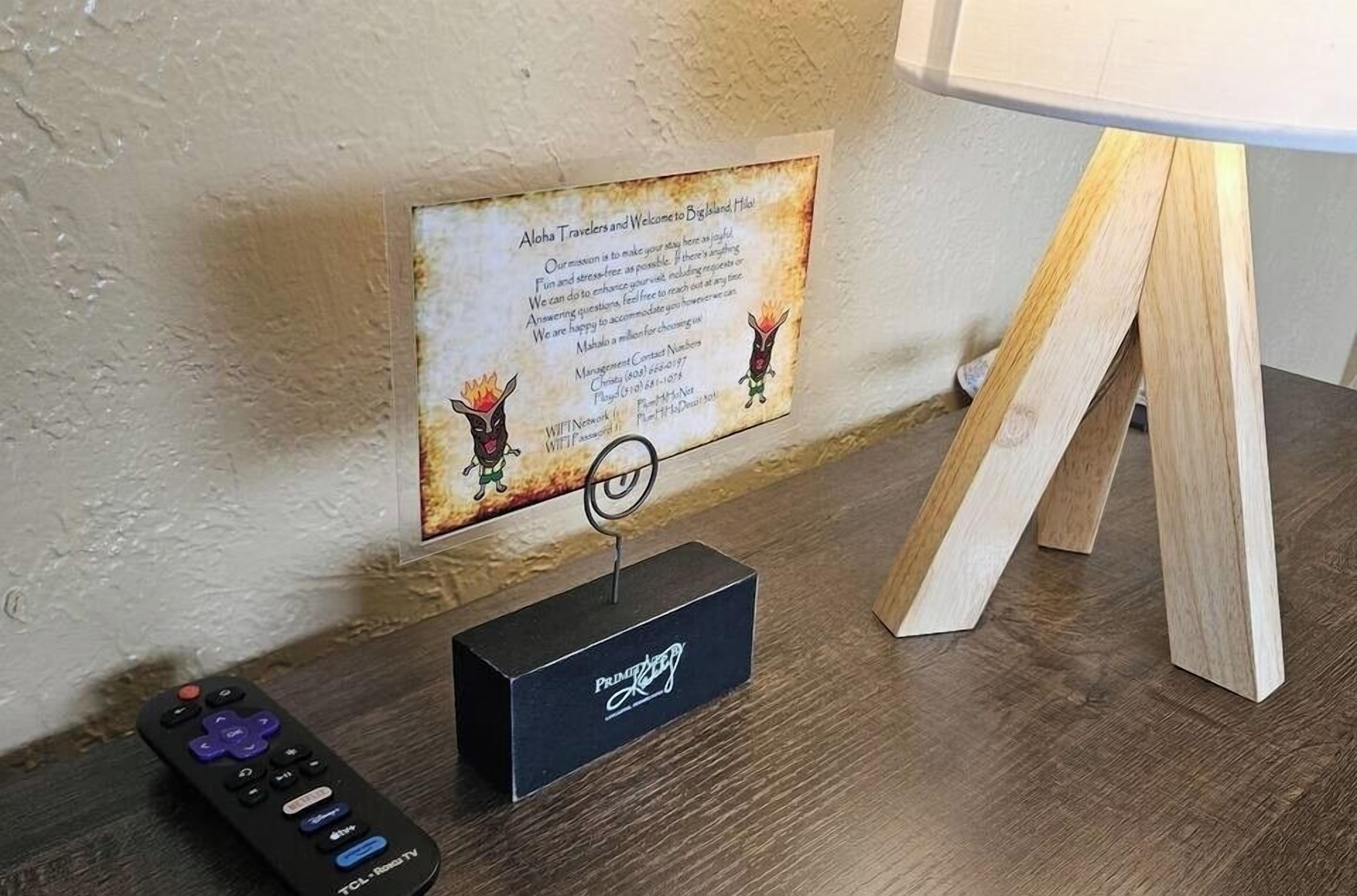 A remote control, a framed welcome sign, and a wooden stand on a wooden table.