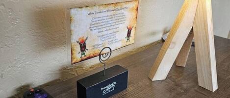 A remote control, a framed welcome sign, and a wooden stand on a wooden table.