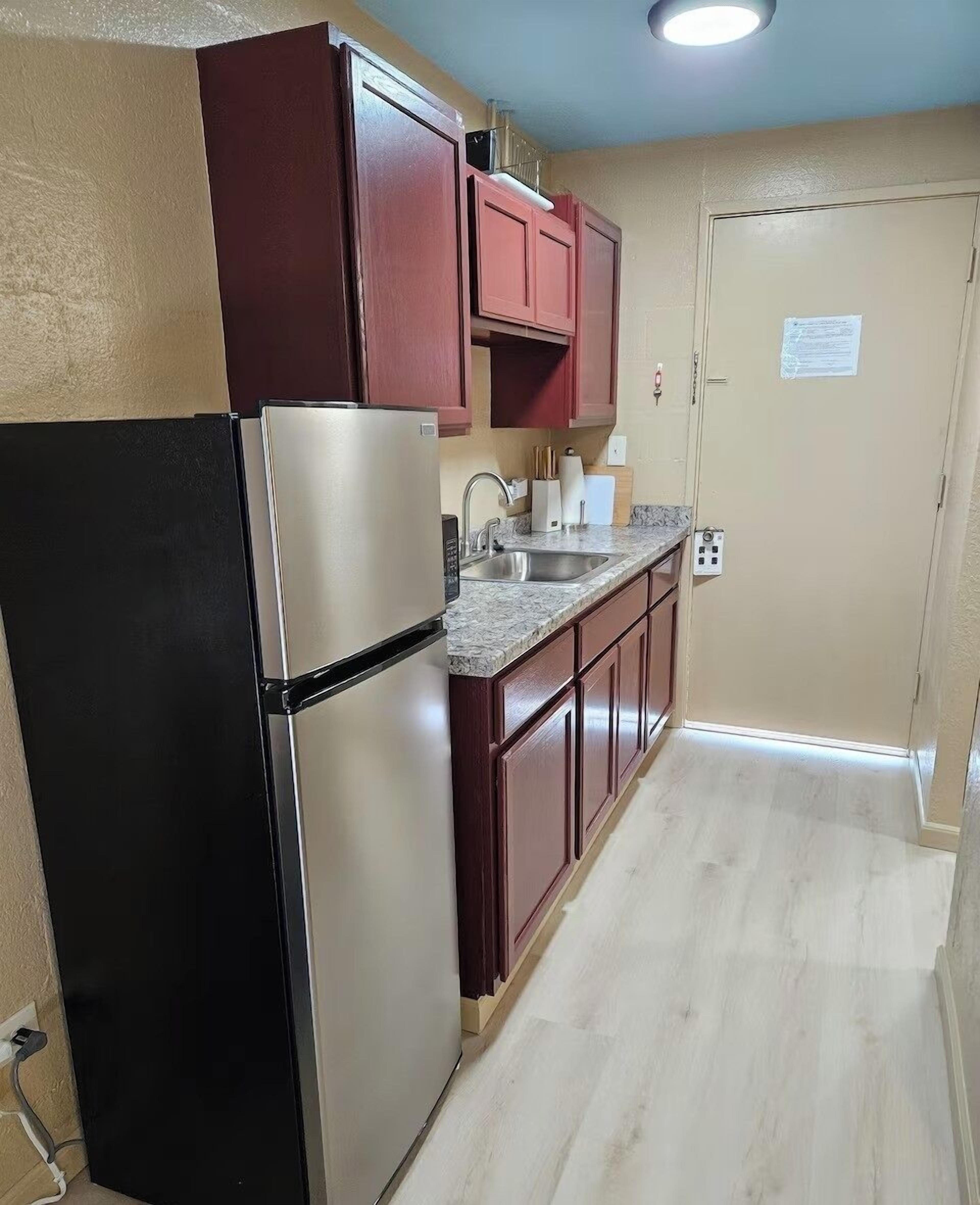 A compact kitchen with a refrigerator, sink, and wooden cabinets.