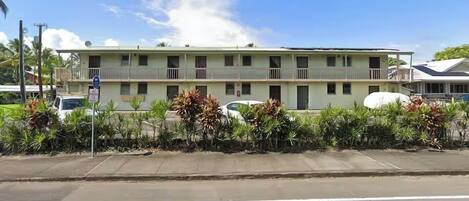 A two-story motel with a flat roof, multiple balconies, and a parking area with cars.