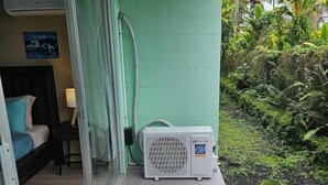 Una stanza con un letto, un comodino, una lampada e una porta scorrevole in vetro che dà su un balcone con un piccolo condizionatore d'aria.