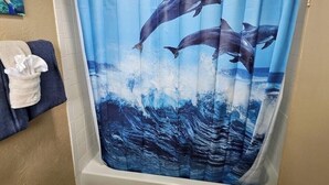 Una tenda da doccia con un motivo di delfini, un portascopino con un asciugamano e un quadro appeso al muro.