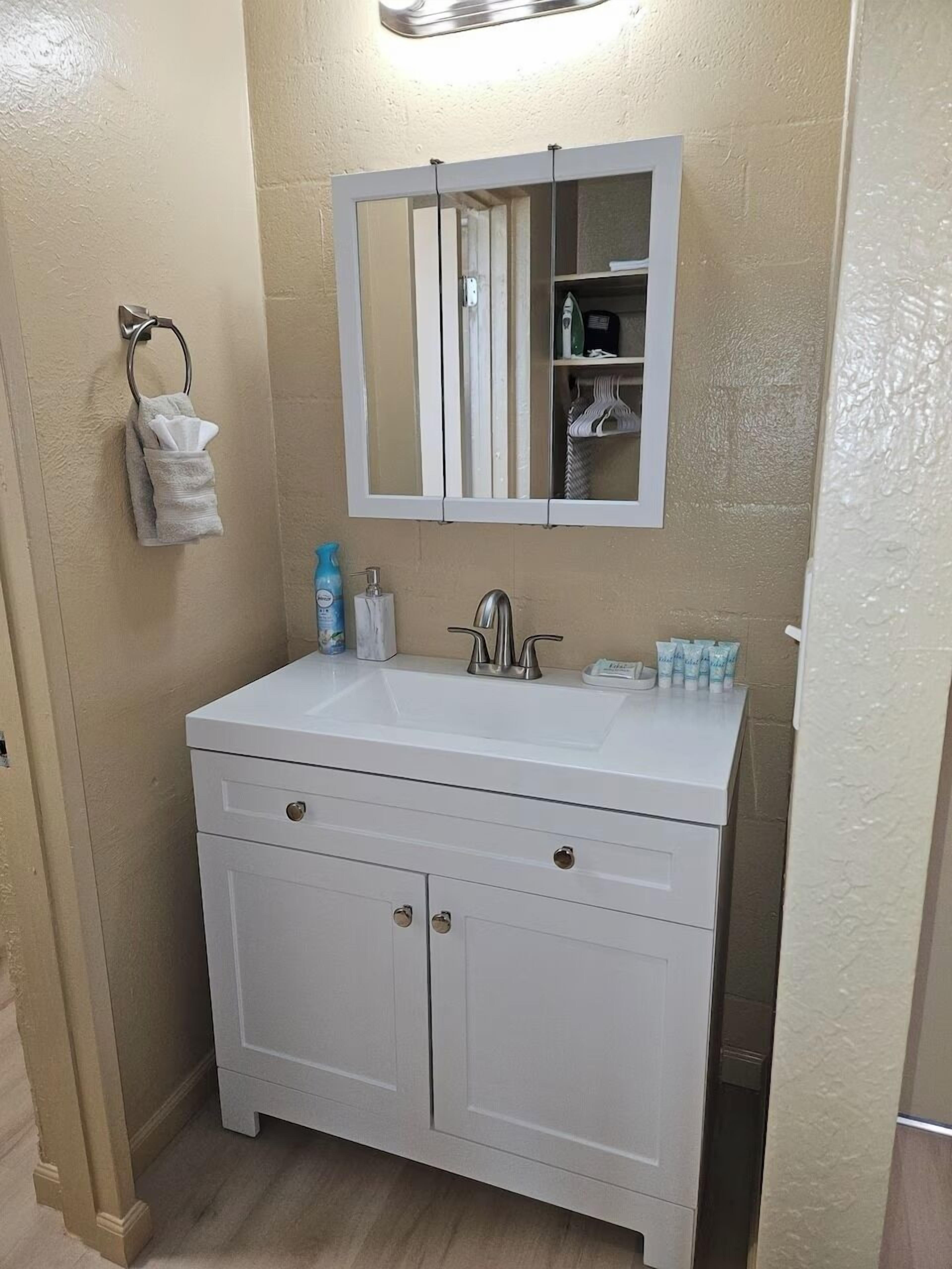 A bathroom with a white vanity, a mirror, a towel rack, and toiletries.