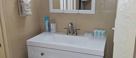 A bathroom with a white vanity, a mirror, a towel rack, and toiletries.