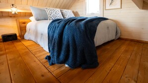 Une chambre avec un plafond en bois, un lit agrémenté d’oreillers à motifs, une couverture bleue et un tableau encadré au mur.