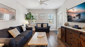 A living room with a dark sofa, a coffee table, a TV, and a ceiling fan. - Residence 102N at The Sandcastle Condominiums (Wildwood Crest)