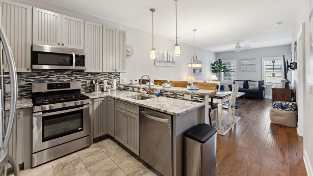 A modern kitchen with stainless steel appliances, a central island, pendant lighting, and a dining area with a view. - Residence 102N at The Sandcastle Condominiums (Wildwood Crest)