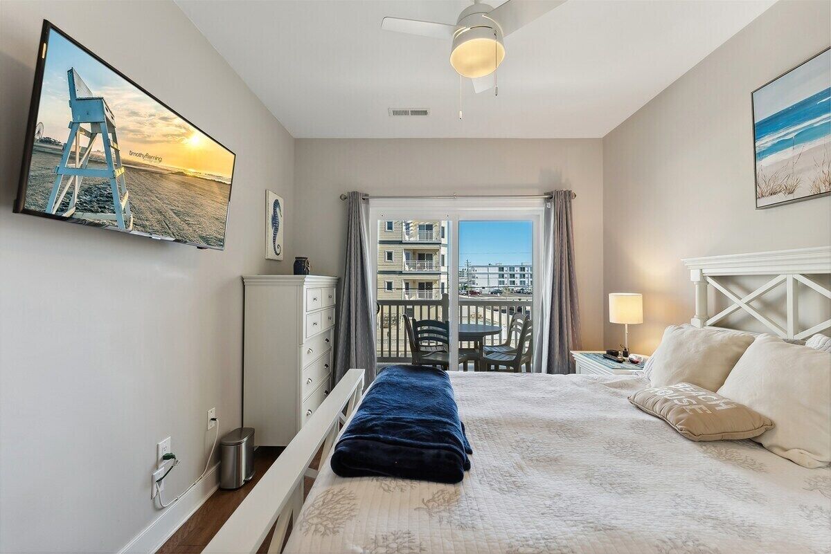 A hotel room with a bed, a desk, a chair, a balcony with a view, and a ceiling fan.