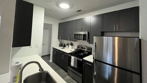 Una cocina moderna con electrodomésticos de acero inoxidable, armarios oscuros y encimera blanca.