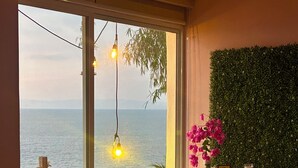 A room with a large sliding glass door leading to a balcony with a view of the sea, a green wall, and a shelf with various items. - Oceanfront Villa-Stunning Sunsets ! (Aguacate)