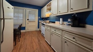 Una cocina con armarios blancos, una estufa y un microondas. Hay una mesa de comedor con sillas.