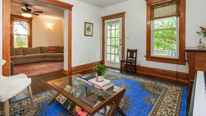 Un salon avec un canapé, une table basse sur laquelle sont posés des livres, un ventilateur de plafond et une grande fenêtre.