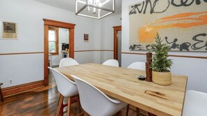 Un coin repas avec une table en bois, des chaises blanches, un lustre et un grand tableau abstrait accroché au mur.