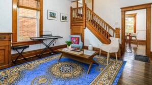 Une pièce avec un escalier en bois, un tapis à motifs bleus, un piano et une chaise.
