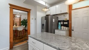 Une cuisine dotée de plans de travail en granit, de meubles blancs, d’un réfrigérateur en acier inoxydable et d’un luminaire suspendu.