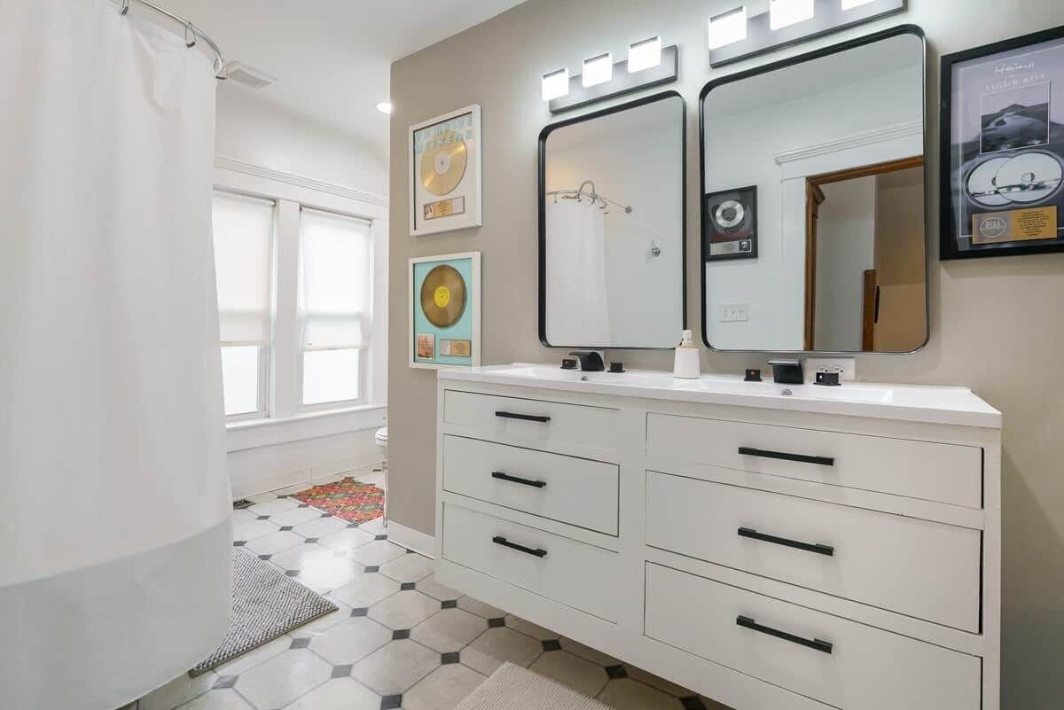 A bathroom with a white vanity, two mirrors, and framed pictures on the wall.