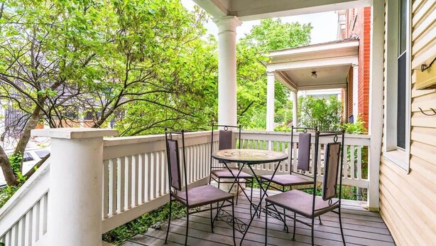 Une véranda avec une table et des chaises, une balustrade blanche et une vue sur des arbres et un bâtiment.