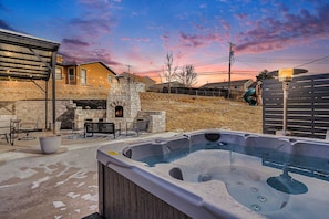 Un jacuzzi en un patio trasero con chimenea de piedra y mobiliario exterior.