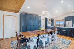 Una cocina moderna con armarios azul oscuro, una mesa de comedor de madera, sillas blancas y una lámpara colgante.