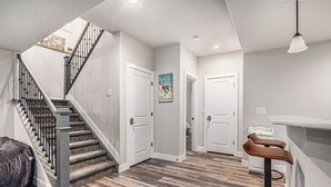 A staircase with a metal railing, a wooden floor, and a bar area with stools. - 5 Bedroom house with amenities galore! Oversized hot tub, outdoor fire pit, smoker and propane grill, sauna, play set, espresso machine, air hockey table, indoor fireplace in both living rooms, and legacy bar. (Colorado Springs)