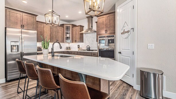 A modern kitchen with a large island, stainless steel appliances, and a 'welcome' sign. - 5 Bedroom house with amenities galore! Oversized hot tub, outdoor fire pit, smoker and propane grill, sauna, play set, espresso machine, air hockey table, indoor fireplace in both living rooms, and legacy bar. (Colorado Springs)