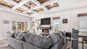 A living room with a large gray sectional sofa, a fireplace, and a mounted TV. - 5 Bedroom house with amenities galore! Oversized hot tub, outdoor fire pit, smoker and propane grill, sauna, play set, espresso machine, air hockey table, indoor fireplace in both living rooms, and legacy bar. (Colorado Springs)