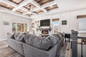 Ein Wohnzimmer mit einem großen grauen Ecksofa, einem Kamin und einem an der Wand befestigten Fernseher.