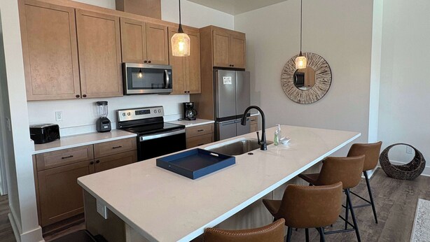 A modern kitchen with wooden cabinets, stainless steel appliances, a central island with bar stools, and a decorative mirror on the wall. - Coastal home near beaches and shopping (Port St. Joe)