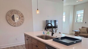 A modern kitchen with a dishwasher, a sink, a round mirror, pendant lights, and a television in the background. - Coastal home near beaches and shopping (Port St. Joe)
