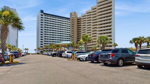 Un estacionamiento con varios coches, un alto edificio de hotel y palmeras.