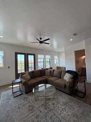 A living room with a sectional sofa, a glass coffee table, and a ceiling fan. - Stylish coastal home near beaches and shopping (Port St. Joe)