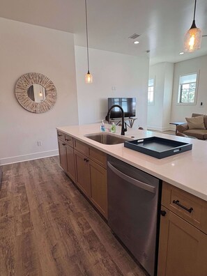 A modern kitchen with a dishwasher, a sink, a round mirror, pendant lights, and a television in the background. - Stylish coastal home near beaches and shopping (Port St. Joe)