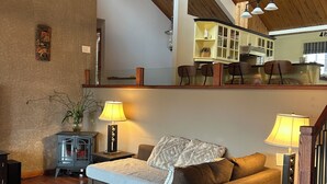 A cozy living room with a sofa, two lamps, a wooden ceiling, and a kitchen in the background.