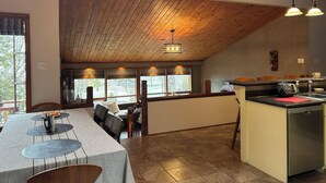 A dining area with a high ceiling, wooden beams, and large windows.