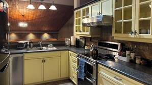 A kitchen with wooden ceiling beams, a stainless steel range, and yellow cabinets.